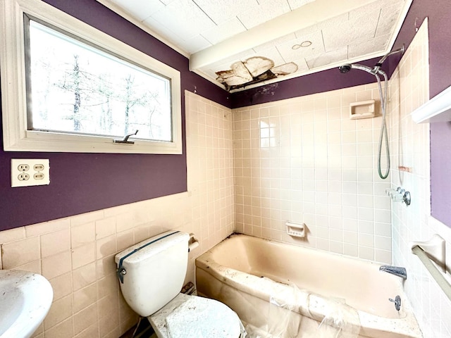 bathroom with tile walls, tiled shower / bath combo, and toilet