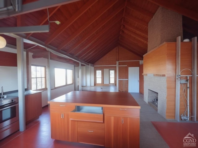 kitchen featuring stainless steel range, high vaulted ceiling, beamed ceiling, a fireplace, and a kitchen island