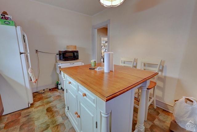 kitchen with a center island, white fridge, white cabinetry, and a breakfast bar area