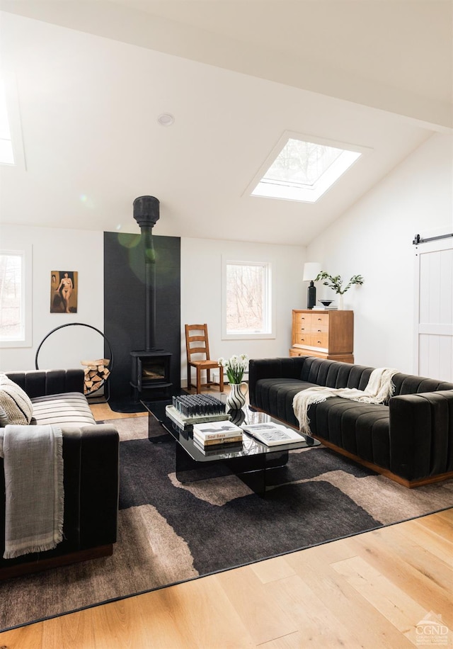 living room with wood finished floors, a wood stove, and vaulted ceiling with skylight
