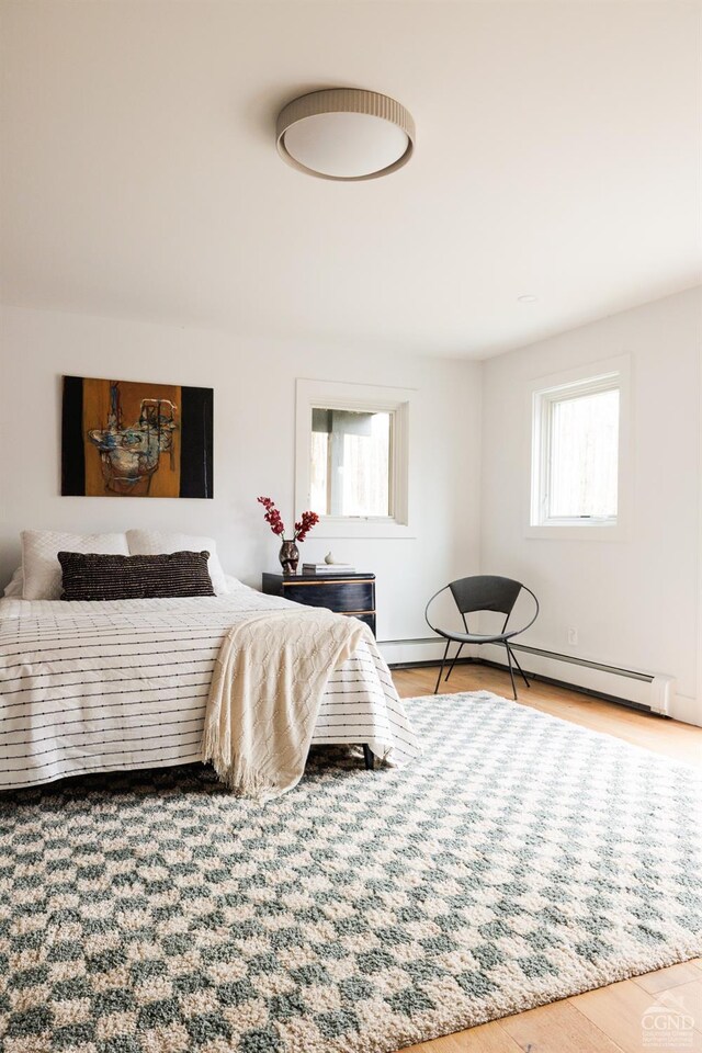 bedroom featuring baseboards, a baseboard heating unit, multiple windows, and wood finished floors
