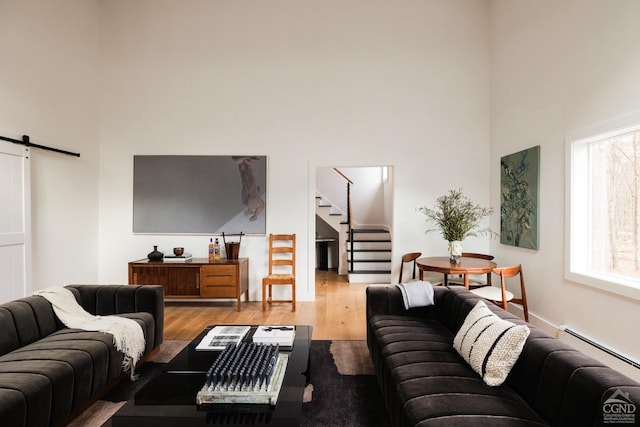 living room featuring wood finished floors, a high ceiling, baseboard heating, stairway, and a barn door