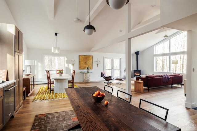 dining area with light wood-type flooring, a wood stove, plenty of natural light, and high vaulted ceiling