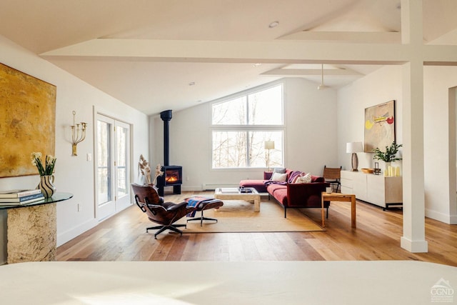 living area featuring lofted ceiling with beams, a wood stove, wood finished floors, and a wealth of natural light