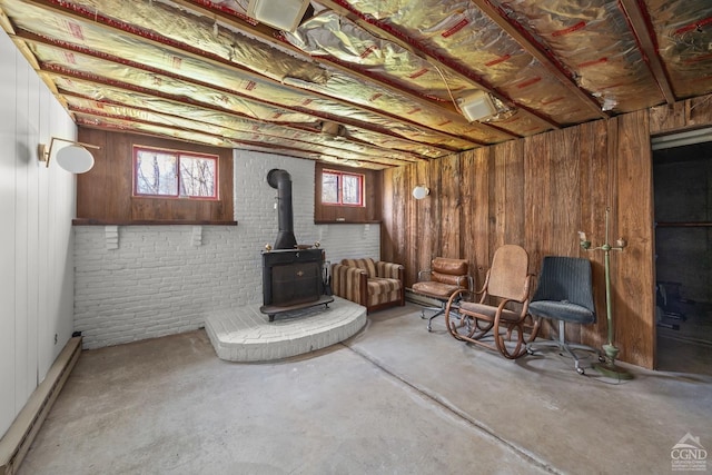 below grade area with a wood stove, a baseboard heating unit, and wooden walls