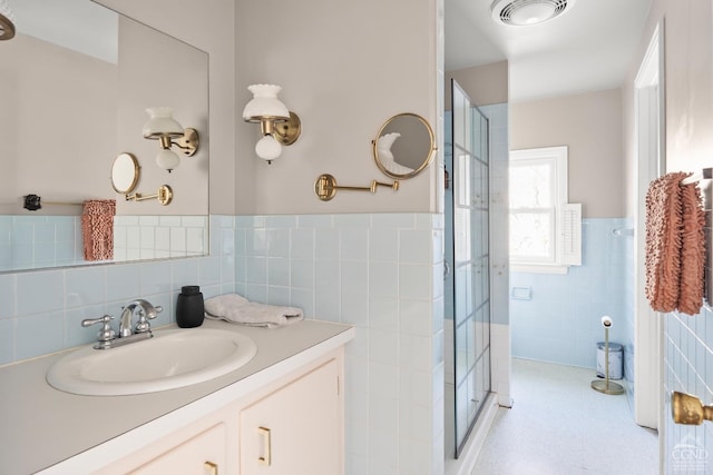full bath featuring vanity, a shower stall, wainscoting, and tile walls