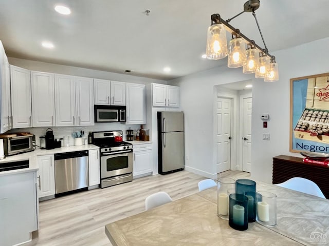 kitchen with light hardwood / wood-style flooring, white cabinets, stainless steel appliances, and decorative light fixtures