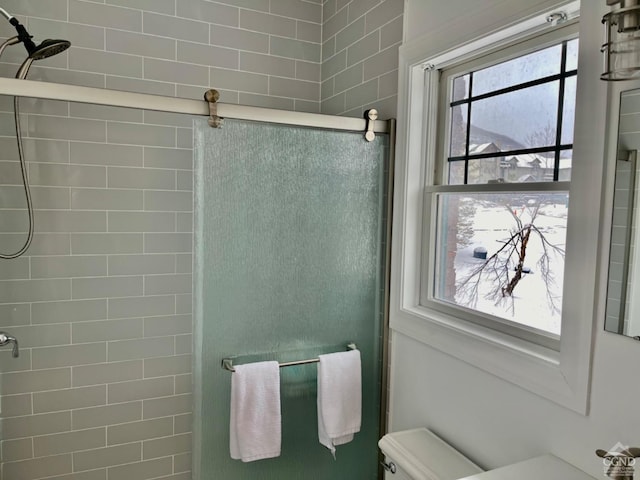 bathroom with a shower with door, toilet, and a wealth of natural light