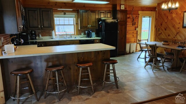 kitchen with a breakfast bar, backsplash, black appliances, sink, and wooden walls