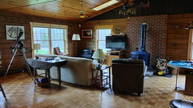 living room with light parquet floors, ceiling fan, lofted ceiling with skylight, a wood stove, and wood walls