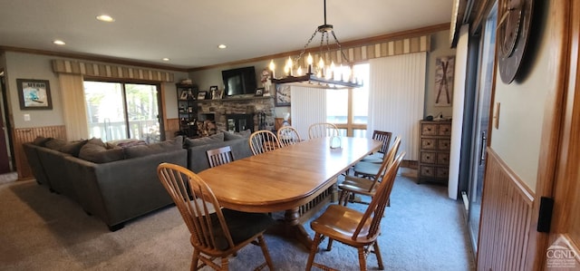 dining room with a wainscoted wall, recessed lighting, a stone fireplace, crown molding, and light colored carpet