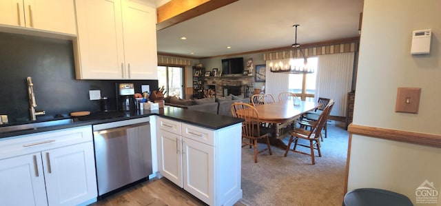 kitchen with dark countertops, a stone fireplace, a peninsula, stainless steel dishwasher, and a sink