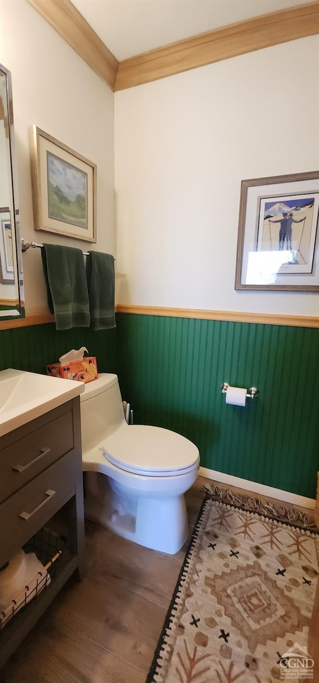 half bathroom featuring vanity, crown molding, toilet, and wainscoting