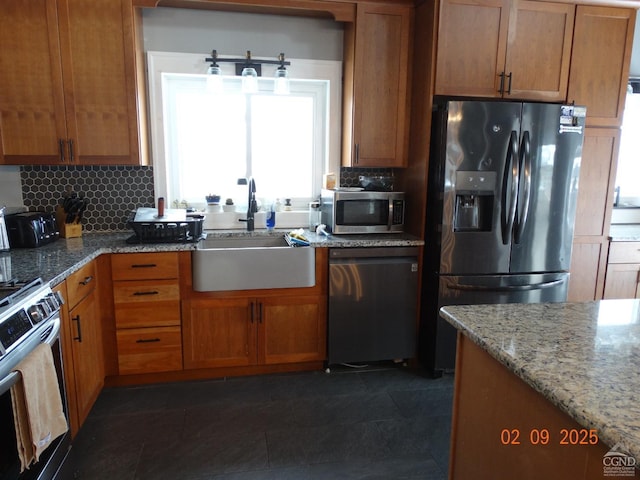 kitchen with sink, light stone counters, dark tile patterned flooring, stainless steel appliances, and decorative backsplash