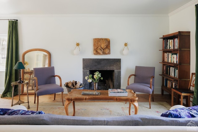 living area featuring baseboards, wood finished floors, ornamental molding, and a fireplace