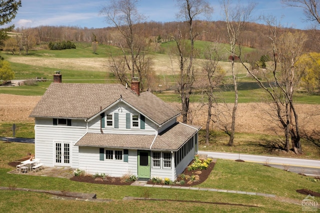 view of front of property with a front yard, a patio area, a chimney, roof with shingles, and french doors