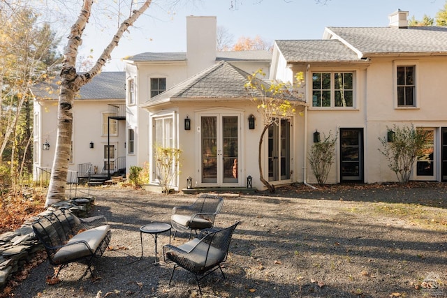 back of house with french doors, stucco siding, a shingled roof, and a chimney