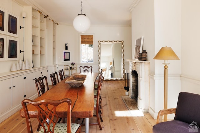 dining area featuring a fireplace, light wood-type flooring, and ornamental molding