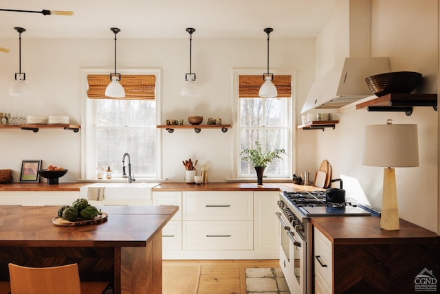 kitchen with sink, wall chimney range hood, wood counters, high end stove, and light hardwood / wood-style floors