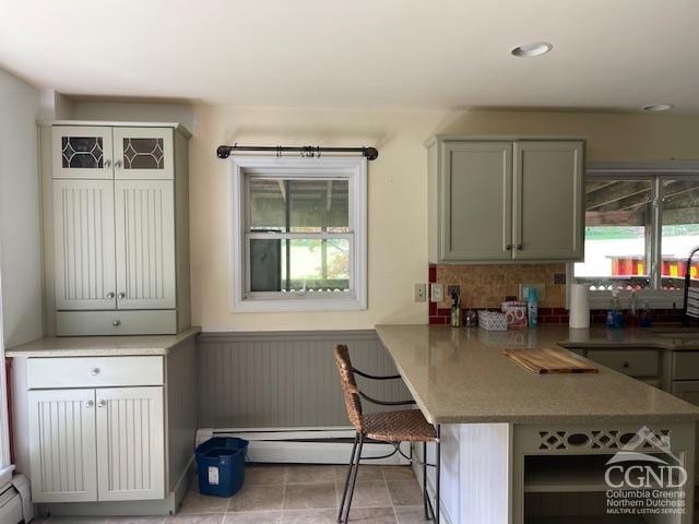 kitchen featuring decorative backsplash, light tile patterned floors, baseboard heating, a kitchen bar, and kitchen peninsula