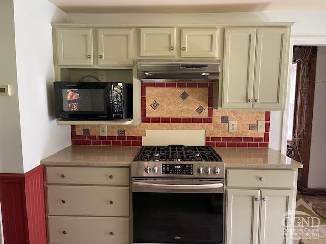 kitchen featuring ventilation hood, tasteful backsplash, cream cabinets, and gas range