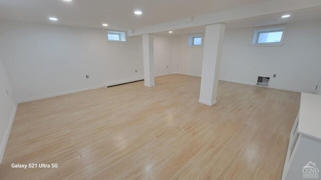 below grade area featuring a baseboard heating unit, recessed lighting, baseboards, and light wood finished floors