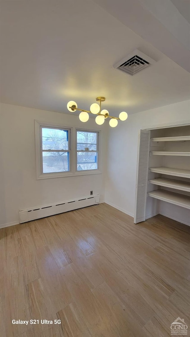 spare room featuring baseboard heating, wood finished floors, visible vents, and baseboards