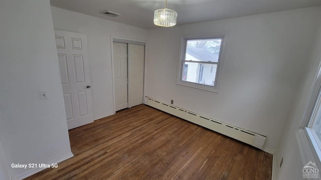 unfurnished bedroom featuring a baseboard radiator, a closet, visible vents, and wood finished floors