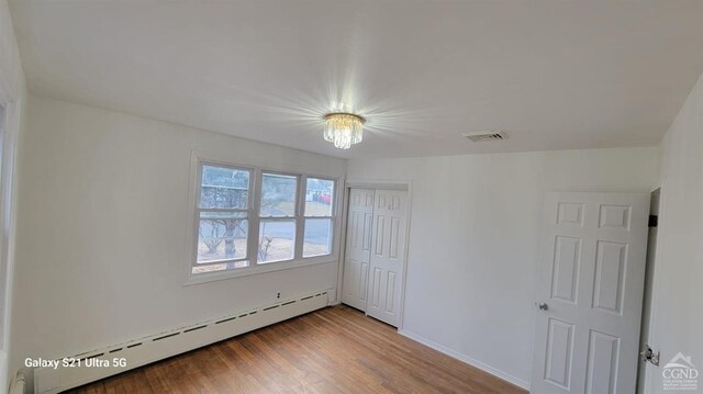 unfurnished room with a baseboard radiator, visible vents, and wood finished floors