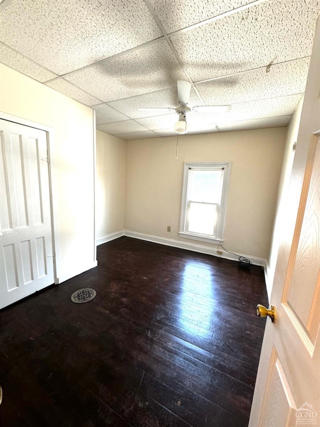 empty room featuring a paneled ceiling, dark hardwood / wood-style floors, and ceiling fan