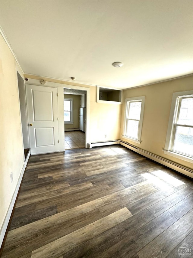 empty room with dark hardwood / wood-style floors, baseboard heating, and a wealth of natural light