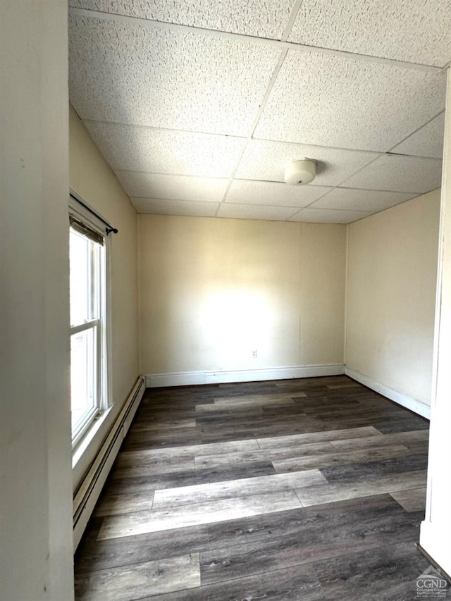 unfurnished room with a drop ceiling, dark wood-type flooring, and a baseboard heating unit