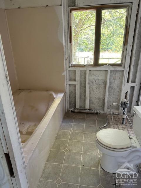 bathroom with a tub to relax in and toilet