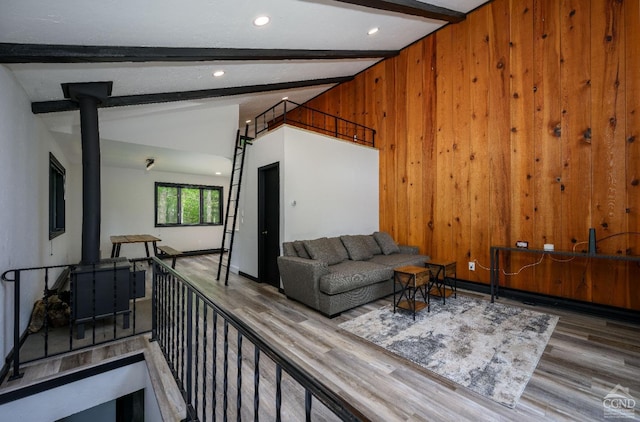 living room featuring a wood stove, wooden walls, wood-type flooring, and vaulted ceiling with beams