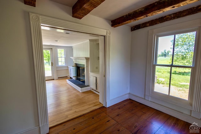 unfurnished living room featuring baseboard heating, hardwood / wood-style floors, and beamed ceiling