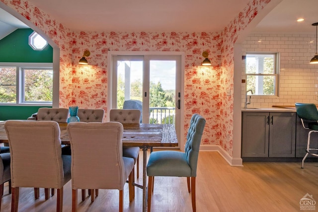 dining space with light wood-type flooring, vaulted ceiling, a wealth of natural light, and sink