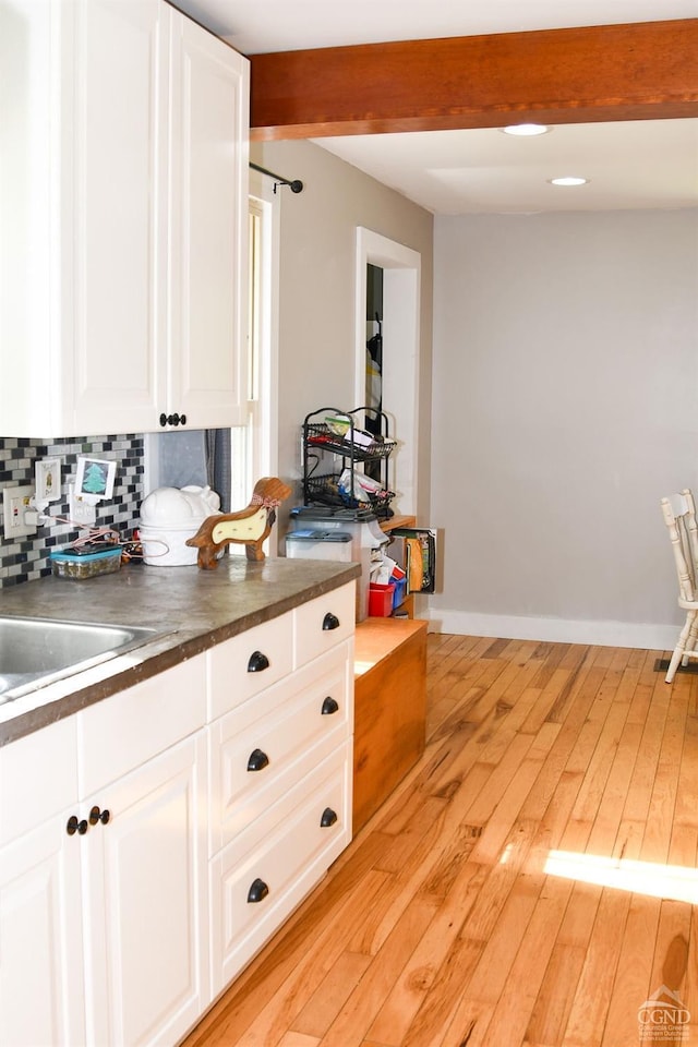 kitchen featuring white cabinets, decorative backsplash, light hardwood / wood-style floors, and beamed ceiling