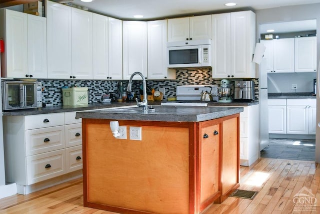 kitchen featuring a center island with sink, white cabinetry, white appliances, and light hardwood / wood-style flooring