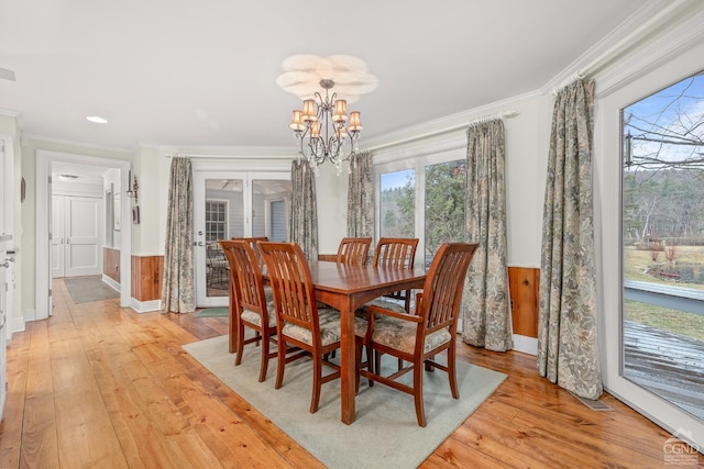 dining space featuring a wainscoted wall, ornamental molding, and an inviting chandelier