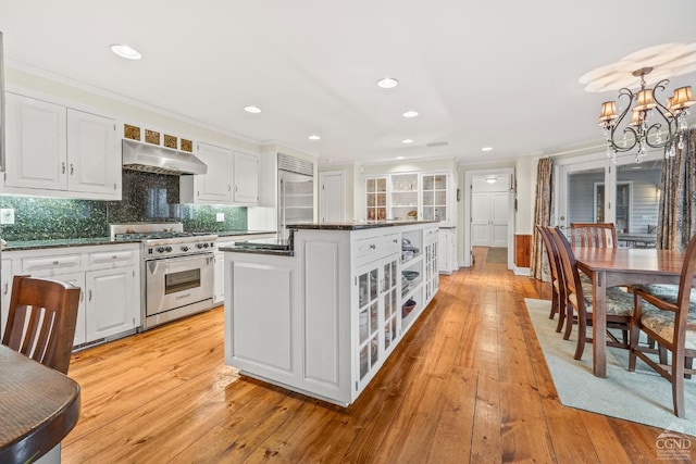 kitchen with high quality appliances, a kitchen island, exhaust hood, white cabinets, and an inviting chandelier