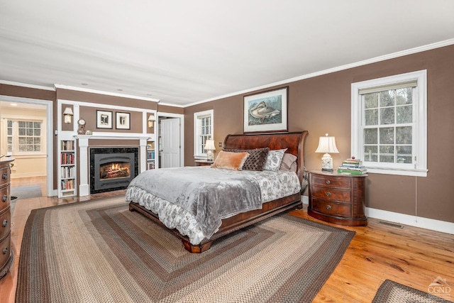 bedroom with ornamental molding, baseboards, a high end fireplace, a closet, and wood finished floors