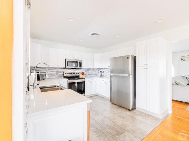 kitchen with sink, white cabinetry, appliances with stainless steel finishes, kitchen peninsula, and decorative backsplash