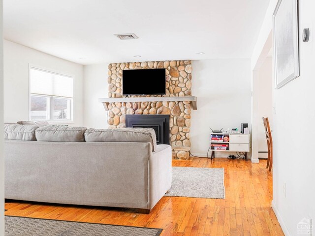 living room with hardwood / wood-style flooring, a stone fireplace, and a baseboard heating unit