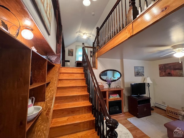 stairs with ceiling fan, wood-type flooring, baseboard heating, and vaulted ceiling