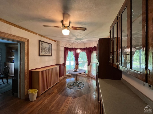 unfurnished dining area featuring ceiling fan, dark hardwood / wood-style flooring, a textured ceiling, and ornamental molding