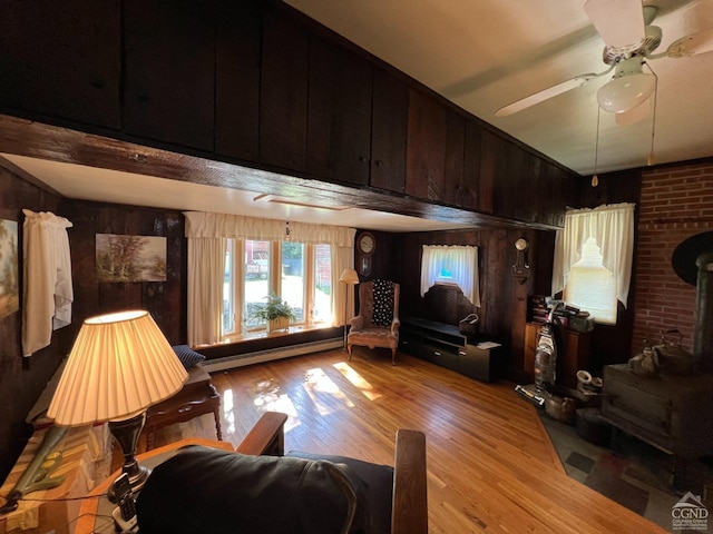 living room with ceiling fan, wood walls, light wood-type flooring, and baseboard heating