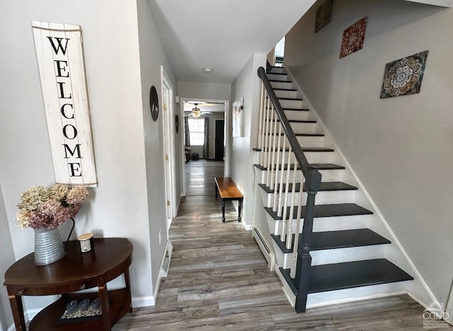 staircase featuring wood-type flooring, a baseboard heating unit, and ceiling fan