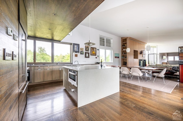 kitchen featuring dark hardwood / wood-style floors, oven, hanging light fixtures, and an island with sink