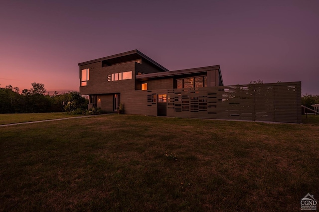 back house at dusk featuring a lawn