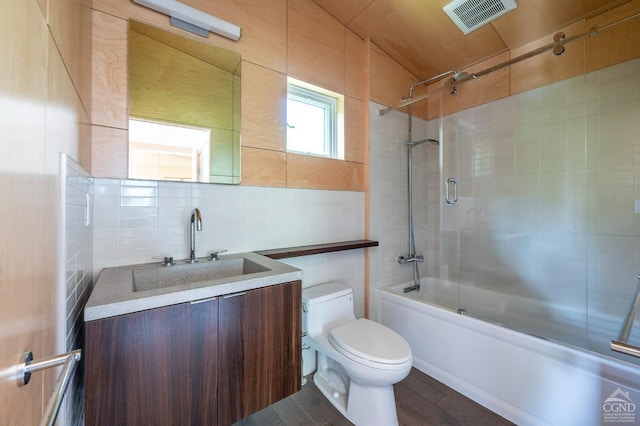 full bathroom with hardwood / wood-style floors, bath / shower combo with glass door, toilet, vanity, and tile walls